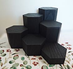 five black wooden cubes sitting on top of a floral tablecloth covered floor next to a white wall