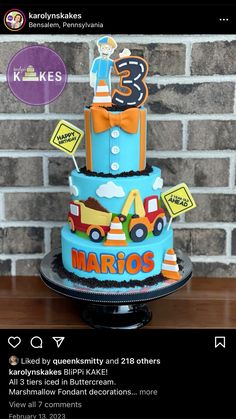 a three tiered cake decorated with cars and street signs is displayed in front of a brick wall