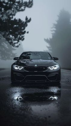 a black car parked in the rain on a wet road with trees and fog behind it