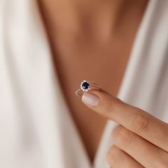 a woman wearing a white shirt holding a ring with a black diamond on it's finger