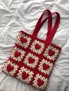 a red and white crocheted bag sitting on top of a bed next to a pillow