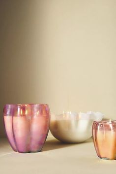 three glass candles sitting next to each other in front of a white bowl on a table