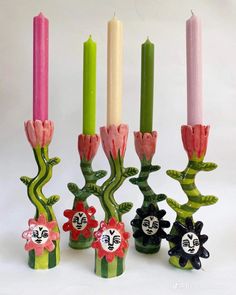 four candles are lined up with flowers and faces on each candle holder in front of them