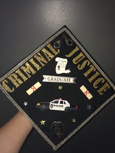 a black graduation cap with gold glitter lettering and police cars on the front is being held up by someone's hand