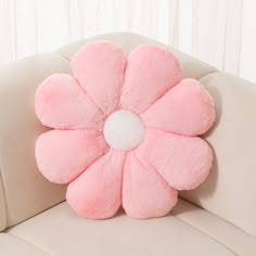 a pink flower shaped pillow sitting on top of a white couch next to a window