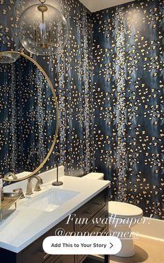 a bathroom with blue and gold wallpaper next to a white sink under a round mirror