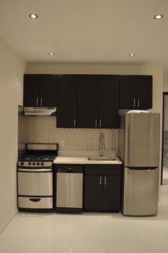 a kitchen with black cabinets and white tile flooring, stainless steel appliances and refrigerator