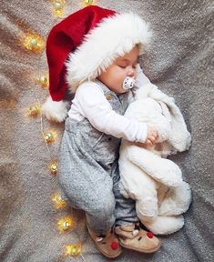 a baby wearing a santa hat sleeping with a stuffed animal