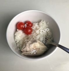 two tomatoes and rice in a white bowl with the same amount of spoons on top