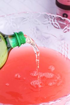 a glass bowl filled with liquid and a green bottle pouring water into the bowl next to it