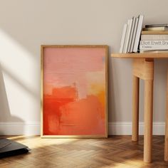 an orange and pink painting sitting on top of a wooden floor next to a table