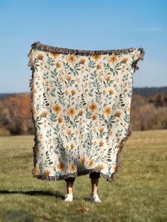 a woman standing in the grass holding up a blanket with sunflowers on it