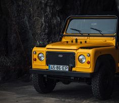 a yellow land rover is parked in front of a rock wall and tree trunk area