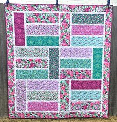 a pink and green quilt hanging on a wooden fence