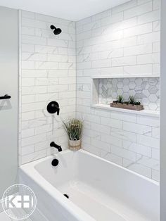 a white bathroom with black fixtures and marble tiles on the walls, along with a plant