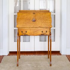 an old wooden desk sitting on top of a rug in front of a white door