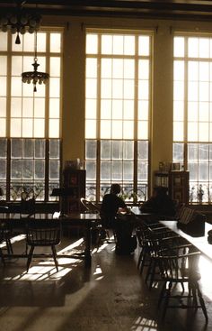 the sun shines through two large windows in a room with many tables and chairs