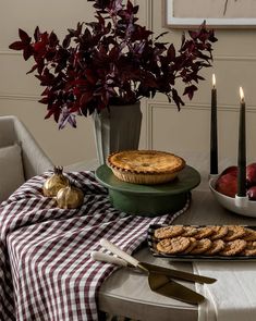 a table topped with pies and cookies next to a vase filled with red flowers