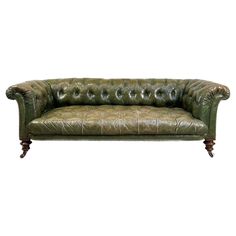 a green leather couch with wooden legs and buttons on the armrests, sitting in front of a white background