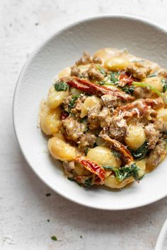 a white bowl filled with pasta covered in meat and vegetables on top of a table