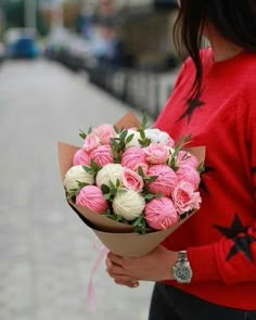 a woman is holding a bouquet of pink and white flowers in her hands while standing on the sidewalk