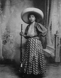 a black and white photo of a woman wearing a hat with a cane in her hand