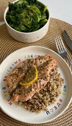 a white plate topped with salmon and rice next to a bowl of salad on top of a table