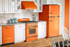 an orange and white kitchen with wood flooring, cabinets, stove top oven and dining room table