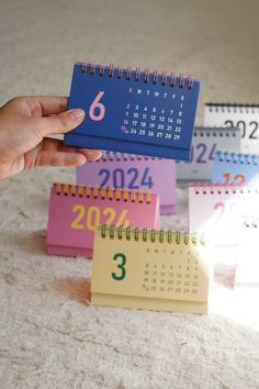 a hand holding a calendar next to three different colored mini calendars on the floor