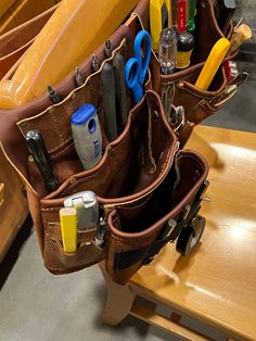 a brown leather tool bag filled with lots of tools and other items sitting on top of a wooden table