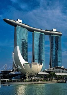 two tall buildings sitting next to each other on top of a body of water with boats in front of them