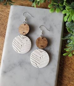 two circular wooden earrings on top of a marble slab next to a potted plant