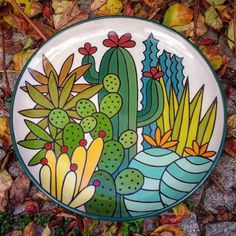 a plate with cactus designs on it sitting in the grass next to leaves and flowers