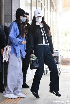 two people wearing face masks are standing on the sidewalk while another person is walking past them