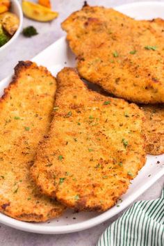 three pieces of fried fish on a white plate next to a bowl of broccoli