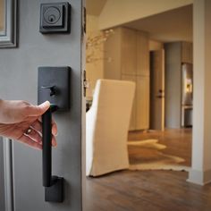 a person's hand is holding the door handle to an open door with a dining room in the background