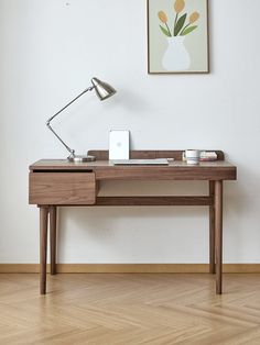 a wooden desk with a lamp on top of it next to a white wall and hardwood floor