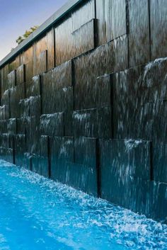 an outdoor swimming pool next to a tall building with water casing on the side