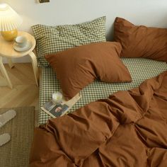 an unmade bed with brown sheets and pillows on top of it next to a small table