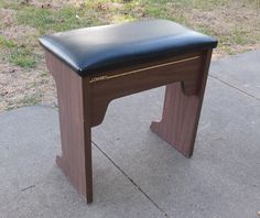 a small wooden bench sitting on top of a cement floor next to a grass covered field