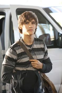 a young man standing in front of a van with his hand on his hip bag