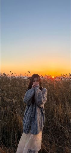 a woman standing in the middle of a field with her hands on her face as the sun sets