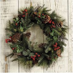 a wreath with pine cones and berries hanging on a white wooden wall, decorated with red berries