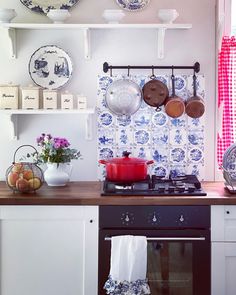 pots and pans are hanging on the wall above an oven in a kitchen with blue and white tiles