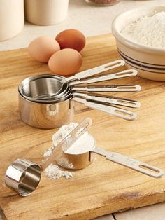 an assortment of kitchen utensils on a cutting board with flour and eggs in the background