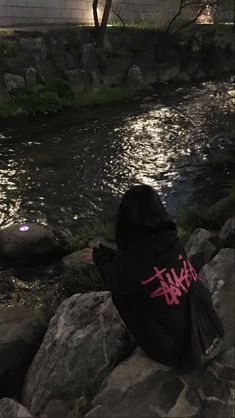 a person sitting on some rocks next to a body of water with graffiti written on it