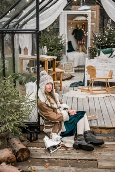 a woman sitting on top of a wooden floor next to a glass house filled with christmas trees