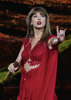 a woman in a red dress holding a microphone and making the peace sign with her hand