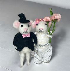 two stuffed animals are standing next to each other with flowers in their hands and one is holding onto another