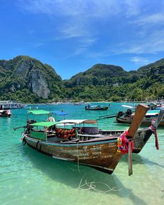 several boats are docked in the clear blue water near some hills and mountains, while one boat is tied up to it's side